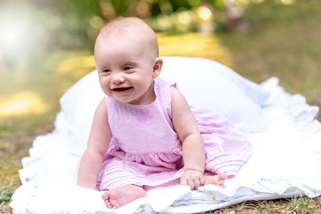 Portrait of cute smiling baby girl sitting outdoors, light effectの写真素材