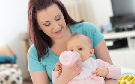 Mother feeding baby girl with bottle at homeの写真素材