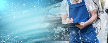 Car mechanic checking a car engine and writing on clipboard; multiple exposureの写真素材