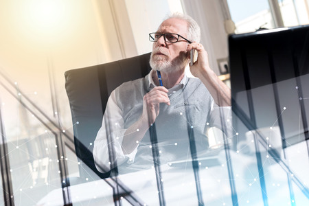 Portrait of bearded senior businessman talking on mobile phone in office, hard light; multiple exposureの写真素材