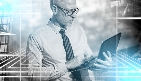 Senior businessman standing and working on his laptop in office; multiple exposureの写真素材