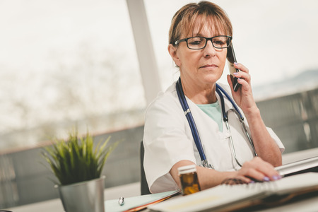 Female doctor talking on mobile phone in medical officeの写真素材