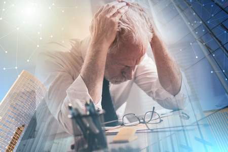Stressed businessman sitting in office with head in hands; multiple exposureの写真素材