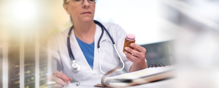 Female doctor holding a bottle of pills in medical office; multiple exposureの写真素材
