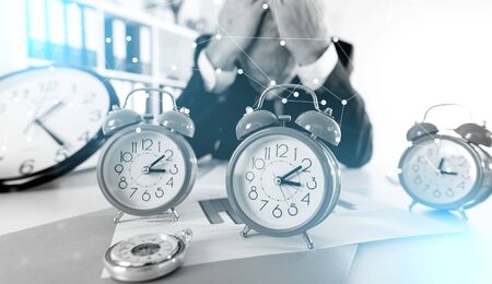 Stressed businessman behind his desk full of alarm clocksの写真素材