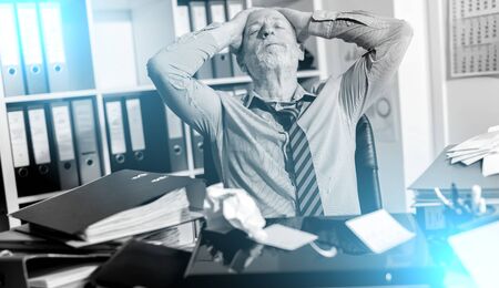 Overworked businessman sitting at a messy desk in office;  light effect