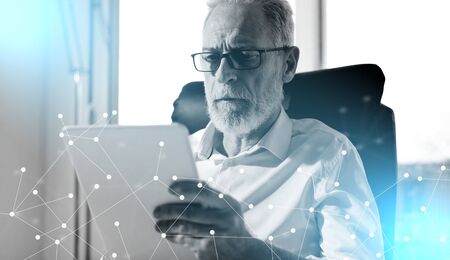 Senior businessman using a digital tablet in office; light effect