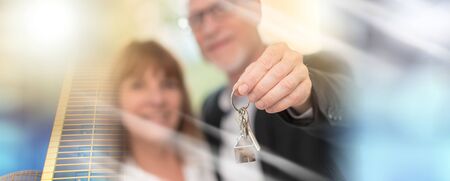 Happy senior couple showing house keys, light effect; multiple exposure