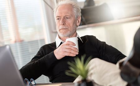 Portrait of senior businessman having coffee break in officeの写真素材