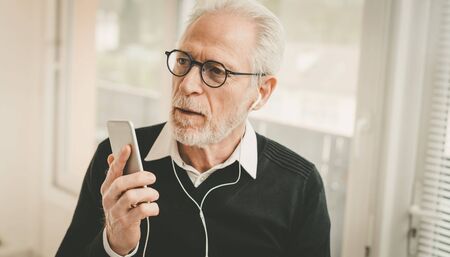Senior businessman using earphones during conversation on mobile phone
