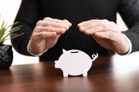 Male hands having a protective gesture of a piggy bank