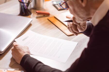 Senior businessman reviewing terms of contract at officeの写真素材