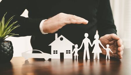 Insurer protecting a family, a house and a car with his handsの写真素材