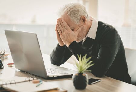 Stressed senior businessman sitting in office with head in handsの写真素材