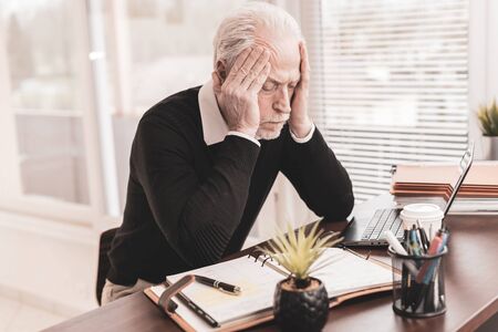 Portrait of overworked senior businessman sitting in officeの写真素材