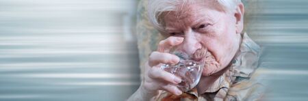 Senior drinking water at home; panoramic banner
