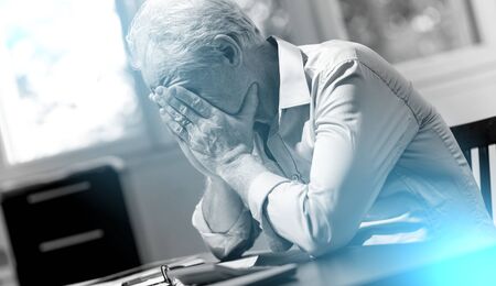 Stressed businessman sitting in office with head in hands; light effectの写真素材