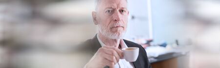 Portrait of senior businessman holding a cup of coffee; panoramic banner