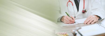 Doctor sitting at desk and taking notes; panoramic bannerの写真素材