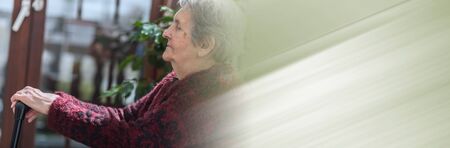 Old woman sitting with her hands on a cane; panoramic bannerの写真素材