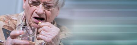 Old woman taking medication at home; panoramic bannerの写真素材