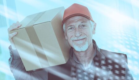 Portrait of smiling senior deliverer holding a package; light effectの写真素材