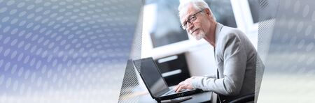 Smiling mature businessman using laptop at office; panoramic banner