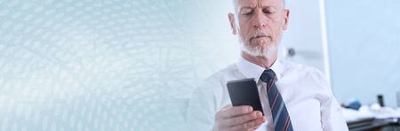 Senior businessman holding his mobile phone at office. panoramic bannerの写真素材