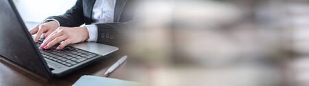 Businesswoman typing on a laptop at office; panoramic banner