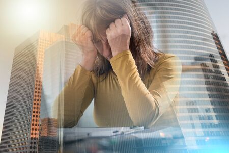 Stressed businesswoman sitting in office with hands on forehead; multiple exposureの写真素材