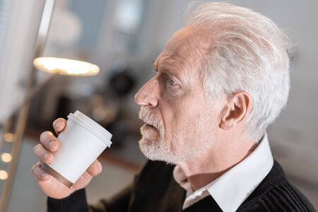 Thoughtful senior man holding a paper coffee cupの写真素材