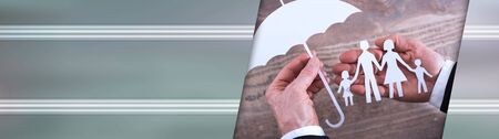 Hands holding a family and an umbrella - insurance concept; panoramic bannerの写真素材