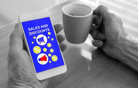 Male hands holding a smartphone with sales and discounts concept and a cup of coffee