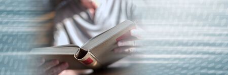 Man sitting at a table reading a book; panoramic banner