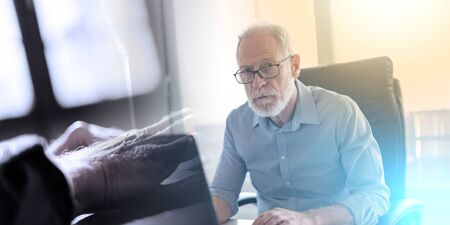 Portrait of senior businessman working on laptop in office; multiple exposure