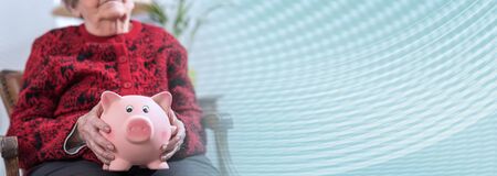 Senior woman holding a piggy bank; panoramic banner