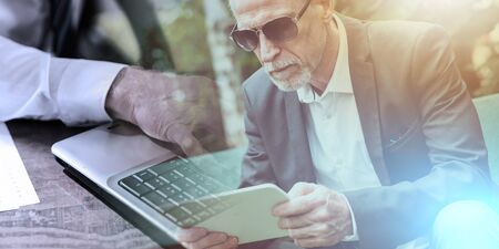 Mature man sitting outdoors and using his tablet; multiple exposureの写真素材