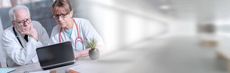Two mature doctors discussing about medical report on laptop; panoramic bannerの写真素材
