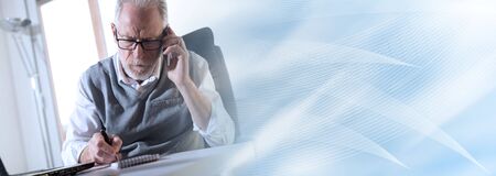 Portrait of senior businessman talking on mobile phone in office; panoramic banner
