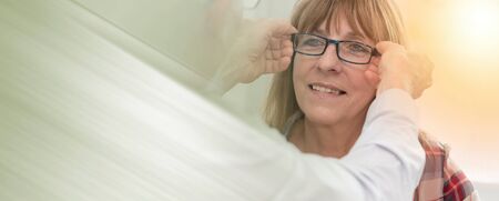 Mature woman testing new eyeglasses in optician store, light effect; panoramic bannerの写真素材