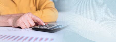 Hands of an accountant working on financial documents and using a calculator; panoramic banner