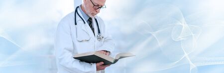 Senior doctor reading a textbook in clinic; panoramic bannerの写真素材