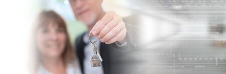 Happy senior couple showing house keys, light effect; panoramic banner