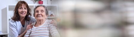 Nurse with her hands on the shoulder of a senior woman; panoramic bannerの写真素材