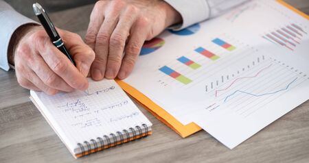 Businessman working on financial results and taking notes on notepad