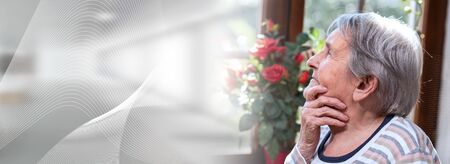 Portrait of elderly woman looking out the window and dreaming; panoramic bannerの写真素材