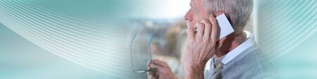 Senior businessman talking on mobile phone and looking through the window; panoramic bannerの写真素材