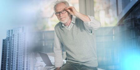 Portrait of smiling senior businessman sitting on his desk in office; multiple exposureの写真素材
