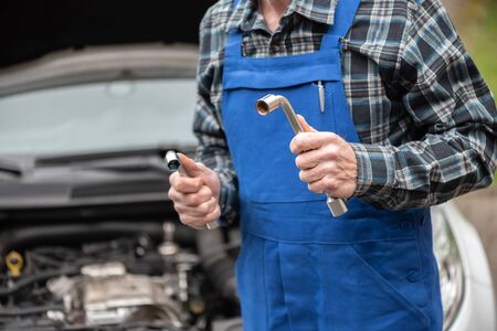 Car mechanic holding tools with car engine on backgroundの写真素材