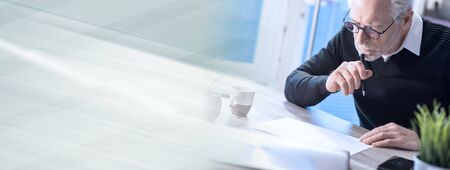 Senior businessÃ£Â¹an working on document at office; panoramic bannerの写真素材